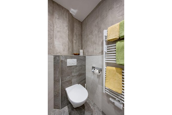 Small, modern bathroom with a white toilet and a towel warmer. The walls are in neutral gray tones and decorated with colorful towels. - Residenz Allegra - Sölden