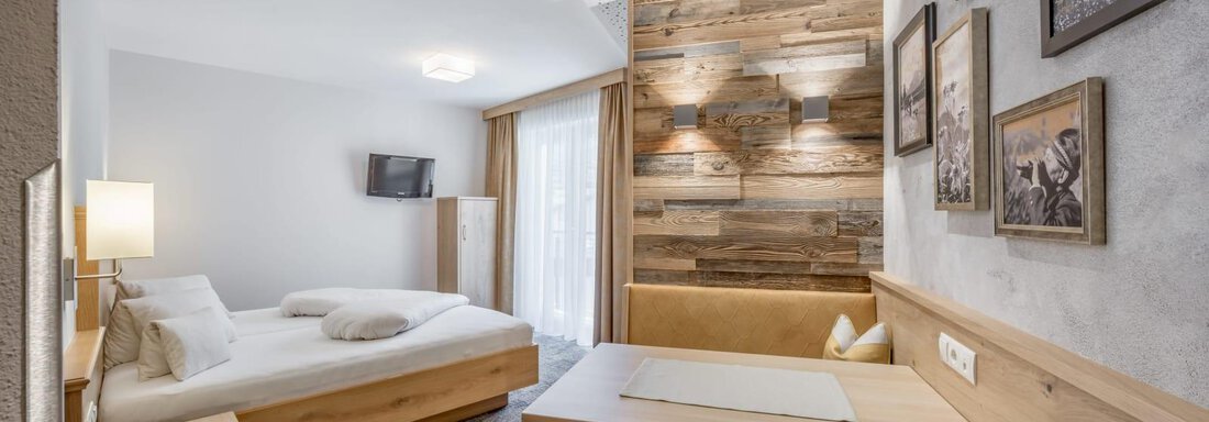 A modern room with a double bed and a cozy dining area. The wooden paneling and the pictures on the wall create an inviting atmosphere. - Residenz Allegra - Sölden