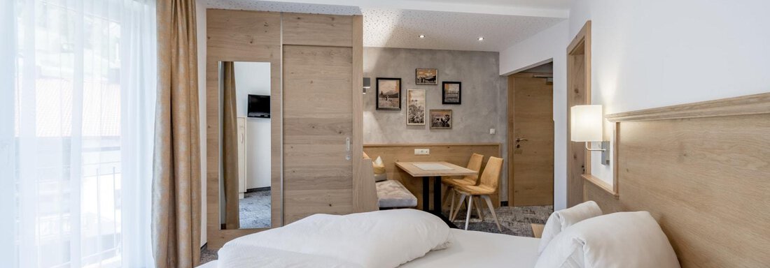A modern hotel room with wooden furnishings and an elegant decor. There is a double bed, a table with chairs, and large windows that let in plenty of light. - Residenz Allegra - Sölden