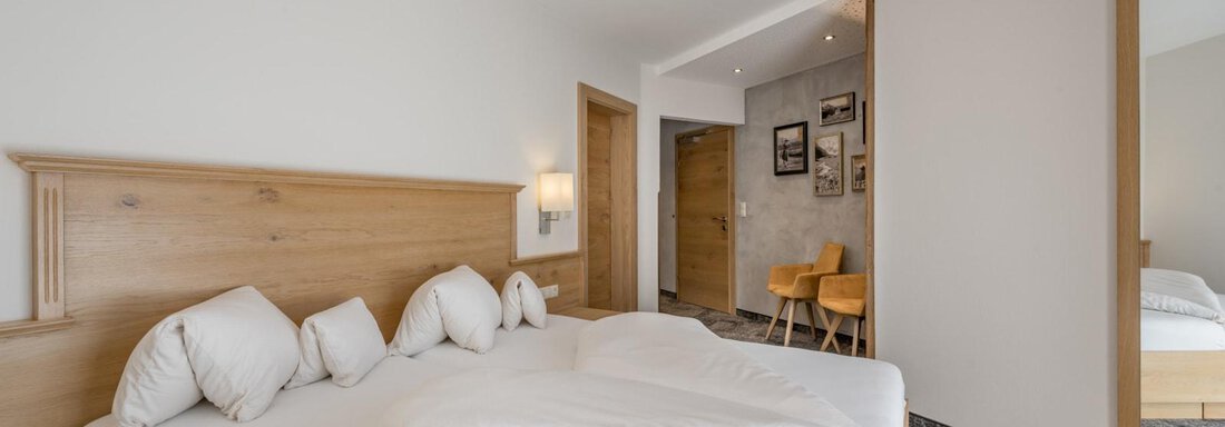 A modern bedroom with a large bed and bright walls. The room is cozily furnished and has a mirror as well as a small table with chairs. - Residenz Allegra - Sölden