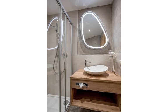 A modern bathroom with a glass shower and an elegant sink. The round mirror with light creates a cozy atmosphere. - Residenz Allegra - Sölden