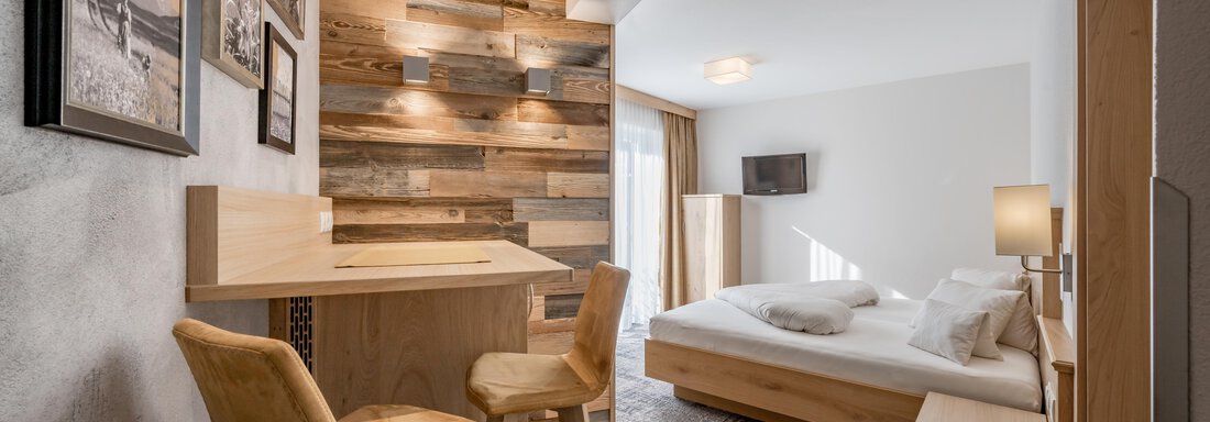 A modern room with a cozy bed and a small seating area. The walls are decorated with wood panels and photos, creating an inviting atmosphere. - Residenz Allegra - Sölden