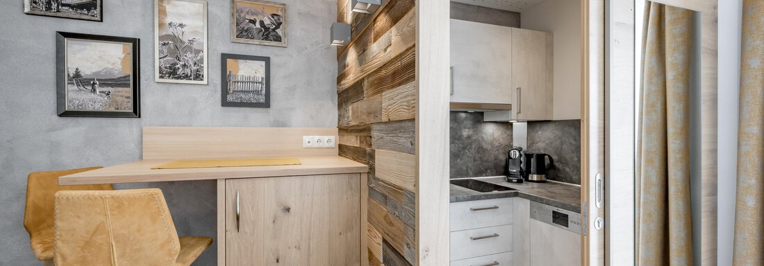 Modern kitchen in a stylish room with wooden paneling and pictures on the wall. A small dining area with stools complements the decor. - Residenz Allegra - Sölden