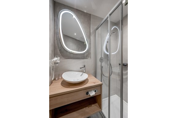 A modern bathroom with a shower and a wooden sink. The mirror has a stylish, illuminated frame. - Residenz Allegra - Sölden
