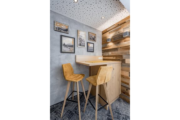 A modern room with a wooden bar and two chairs. Several pictures hang on the wall, and the lighting is subtle. - Residenz Allegra - Sölden
