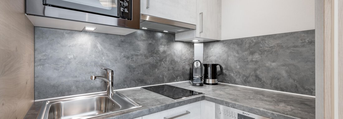 A modern kitchen with a microwave, a refrigerator, and a dishwasher. The countertop is in a gray tone and the cabinets are light. - Residenz Allegra - Sölden
