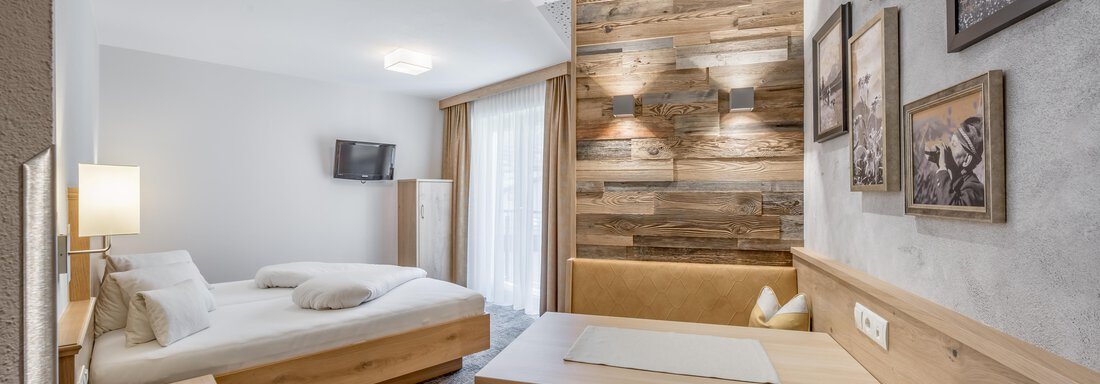A modern hotel room with wooden decor and a cozy setup. The room features a double bed, a table, and a television. - Residenz Allegra - Sölden