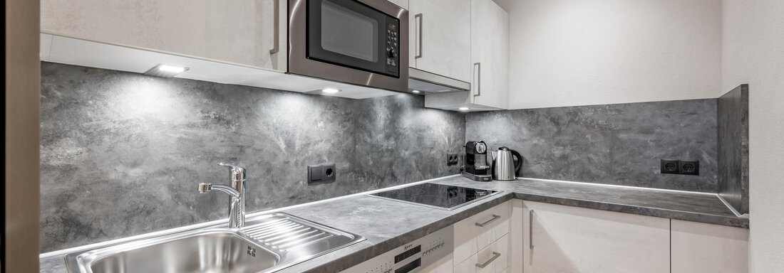 A modern kitchen with gray surfaces and a stainless steel sink. It is well-equipped with a microwave and a kettle. - Residenz Allegra - Sölden