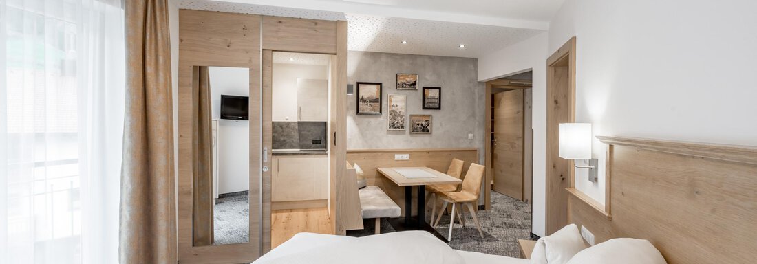 A modern hotel room with a large bed and cozy furnishings. The room features a dining area and large windows that let in plenty of light. - Residenz Allegra - Sölden