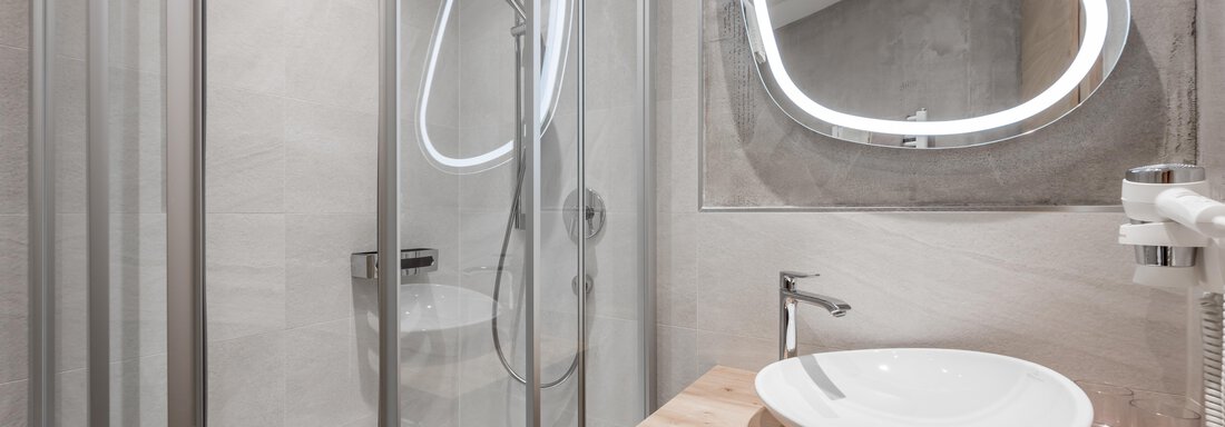 A modern bathroom with a shower, a sink, and an elegant mirror. The walls are in neutral tones, creating a bright and friendly atmosphere. - Residenz Allegra - Sölden