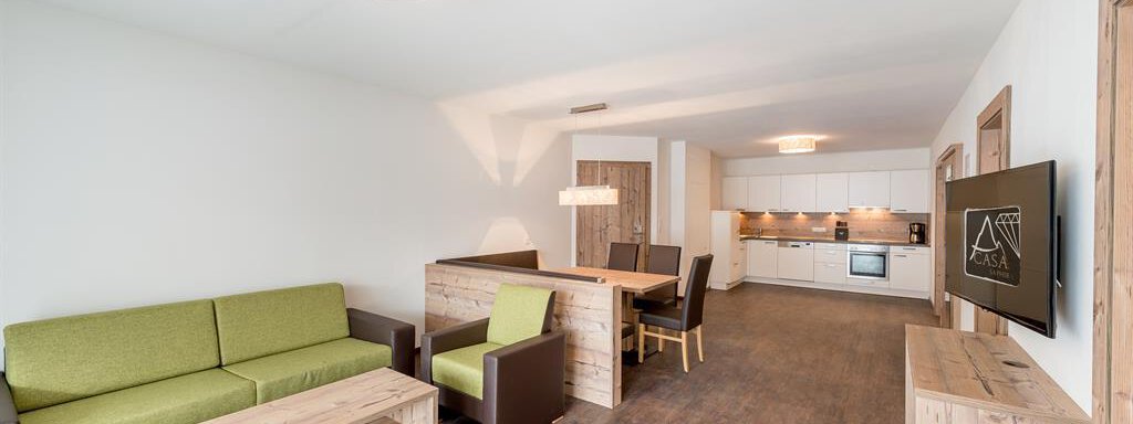 A modern living room with a green sofa and wood paneling. The open kitchenette offers an inviting atmosphere. - Revmatologická poradna Appt Top 4 - Sölden