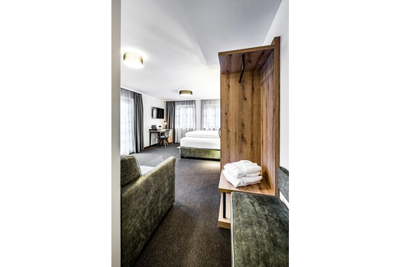 A modern room with a double bed, a desk, and a cozy seating area. The windows are fitted with curtains and let in plenty of daylight. - Sonnalp Residences - Sölden