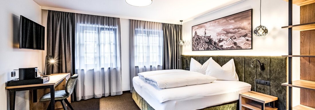 A modern hotel room with a large bed and a desk. Bright curtains let in plenty of light and create an inviting atmosphere. - Sonnalp Residences - Sölden
