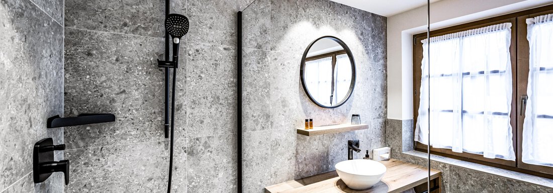 Modern bathrooms with gray stone walls and a shower. On the wooden shelf, there is a sink and decorative items. - Sonnalp Residences - Sölden