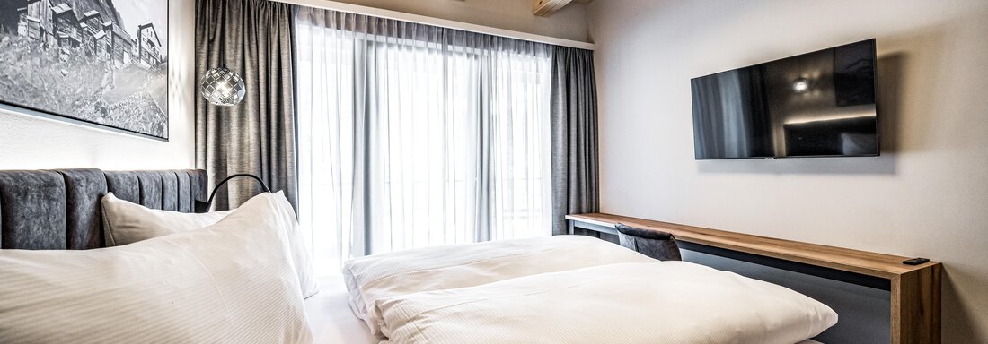 A modern bedroom with wooden ceilings and large windows. The room is bright and well-furnished, with a television and cozy beds. - Sonnalp Residences - Sölden