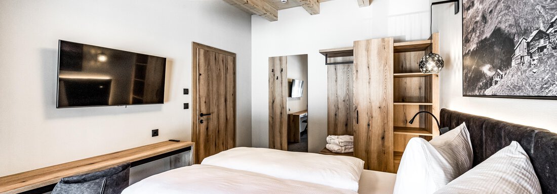 A modern room with a double bed and bright wood design. There is a television, a desk, and a wooden dresser. - Sonnalp Residences - Sölden