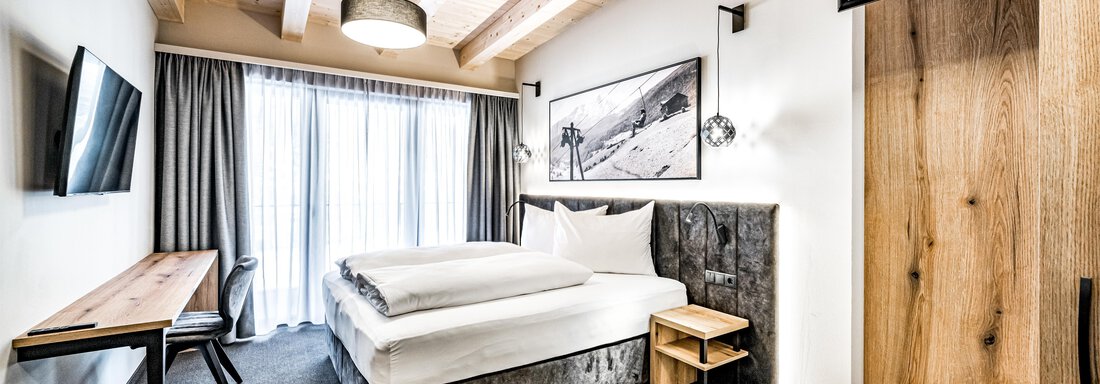 A modern bedroom with a comfortable bed and wooden details. Large windows let in plenty of daylight and create a cozy atmosphere. - Sonnalp Residences - Sölden