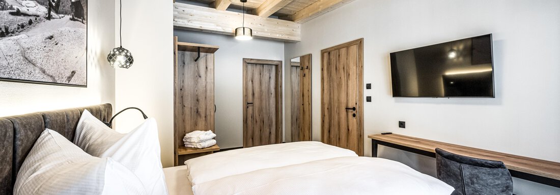 A modern bedroom with two beds and a wooden ceiling. A television hangs on the wall and there is a small desk. - Sonnalp Residences - Sölden