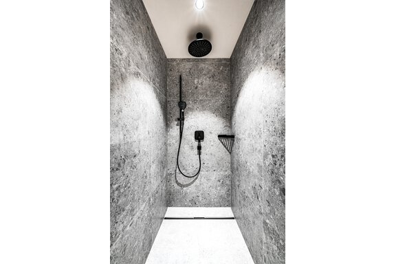 A modern shower with gray stone walls and a black shower fixture. The lighting creates a bright atmosphere. - Sonnalp Residences - Sölden