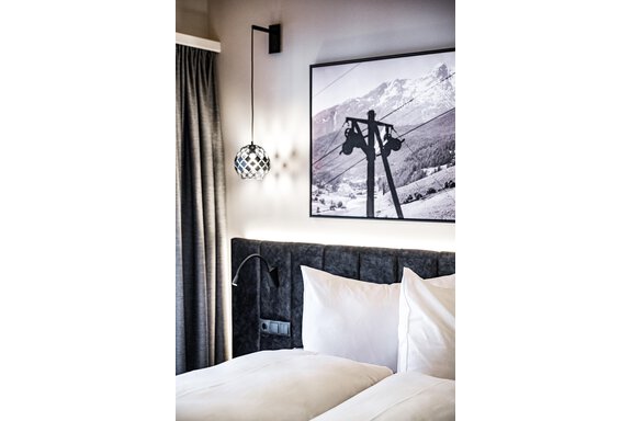 A modern bedroom with two beds and white pillows. On the wall hangs a black-and-white picture of a cable car in the mountains. - Sonnalp Residences - Sölden