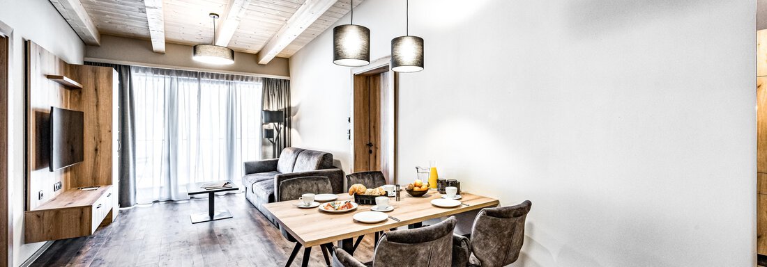 A modern living and dining room with a wooden floor and large windows. The dining area is furnished with a table and comfortable chairs. - Sonnalp Residences - Sölden
