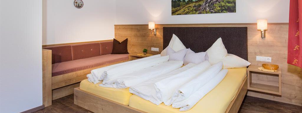 A cozy bedroom with a large bed and wooden paneling. A picture of a mountain landscape hangs on the wall. - Sportpension Rubin - Sölden