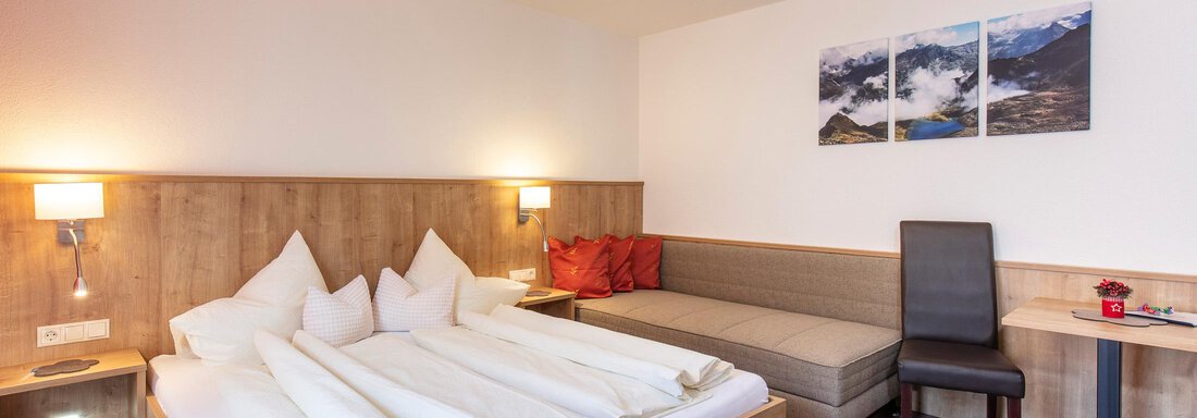 A cozy bedroom with a double bed and a seating area. The walls are bright, and there are decorative pictures that show the surroundings. - Sportpension Rubin - Sölden