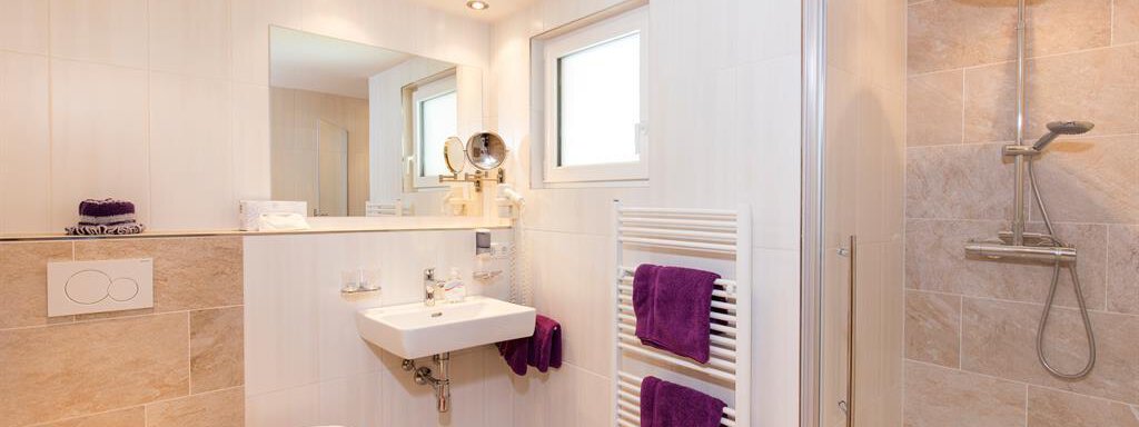 A modern bathroom with a shower and a sink. The walls are bright and the design is simple and elegant. - Sportpension Rubin - Sölden