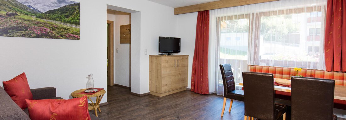 A cozy living space with a gray sofa and a dining table. Large windows let in plenty of light and provide a view of the surroundings. - Sportpension Rubin - Sölden