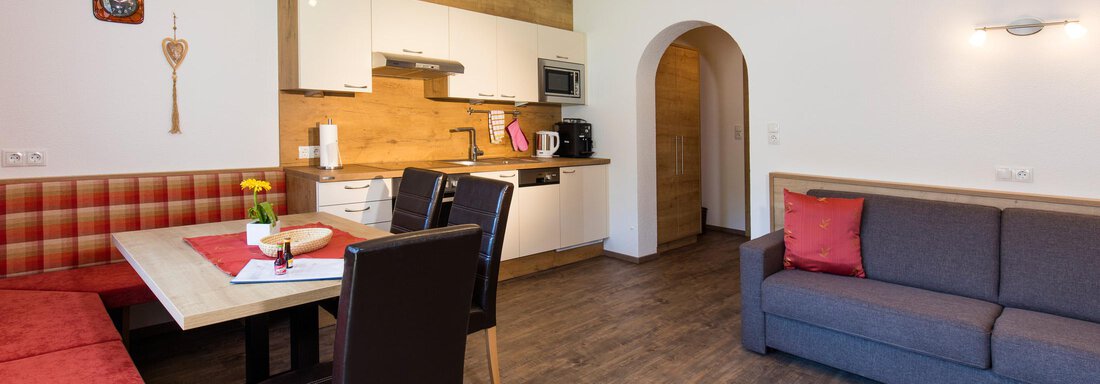 A modern kitchen-living room with a seating area and a cozy sofa. The wooden details give the room an inviting atmosphere. - Sportpension Rubin - Sölden