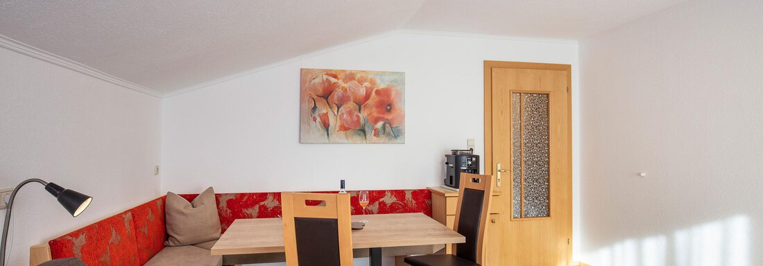 A cozy living area with a dining space and a red bench. The walls are light and a decorative picture is visible. - Sportpension Rubin - Sölden