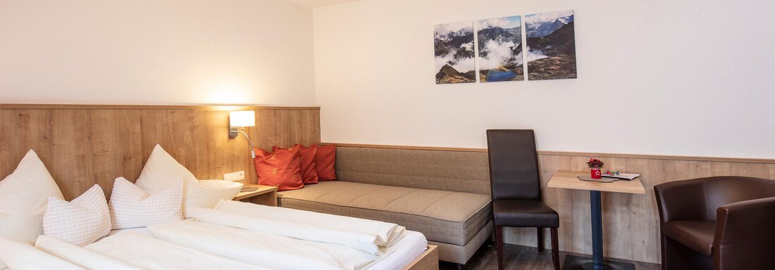 A cozy hotel room with two beds, a seating area, and modern furniture. Pictures of mountains hang on the wall. - Sportpension Rubin - Sölden