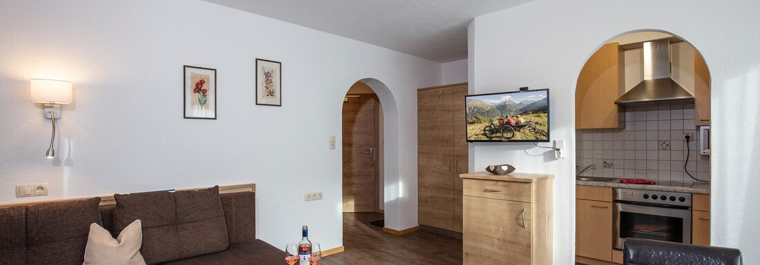 A cozy living space with a couch, a table, and a television. The walls are light, and there are some decorative pictures. - Sportpension Rubin - Sölden