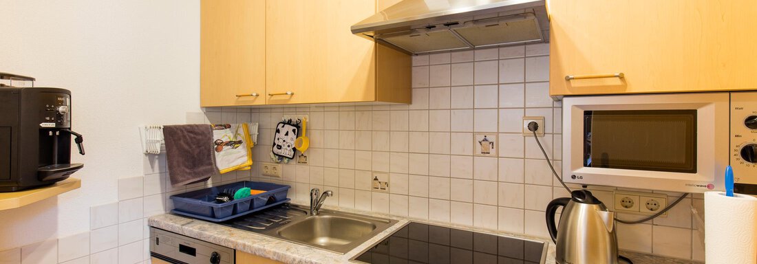A modern kitchen setup with wooden cabinets and stainless steel appliances. The kitchen unit includes a stove, a sink, and a microwave. - Sportpension Rubin - Sölden
