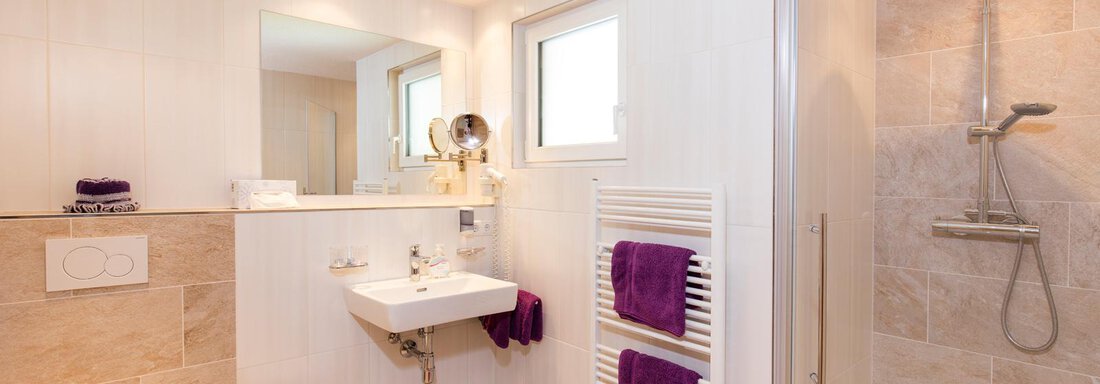 A modern bathroom with a shower, sink, and toilet. Towels in purple colors provide an elegant accent. - Sportpension Rubin - Sölden