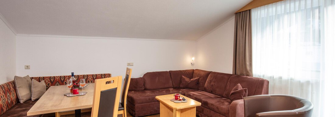 A cozy living space with a sitting area and a dining table. Large windows let in plenty of light and create an inviting atmosphere. - Sportpension Rubin - Sölden