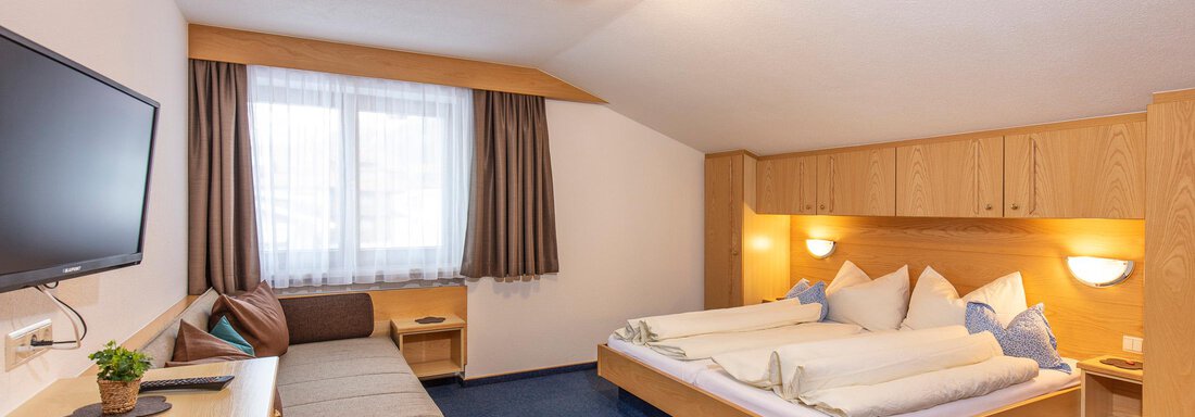 A modern bedroom with two single beds and a cozy seating area. The windows let in plenty of daylight and the decor is simple and inviting. - Sportpension Rubin - Sölden