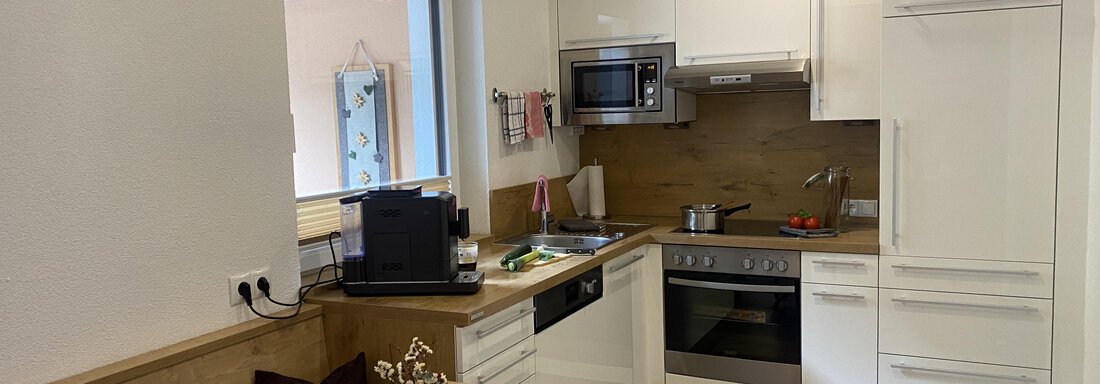 A modern kitchen with bright furniture and a wooden table. There is a fruit bowl on the table. - Sportpension Rubin - Sölden