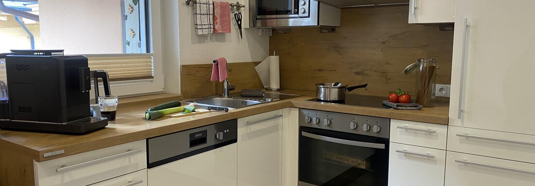 A modern kitchen with white cabinets and wood details. Fresh vegetables and a coffee machine are on the countertop. - Sportpension Rubin - Sölden