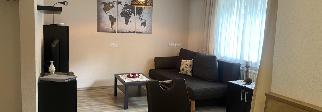 livingroom small but smart A modern living room with a cozy sofa and a table. A world map hangs on the wall, and there are large windows that let in plenty of light. - Sportpension Rubin - Sölden