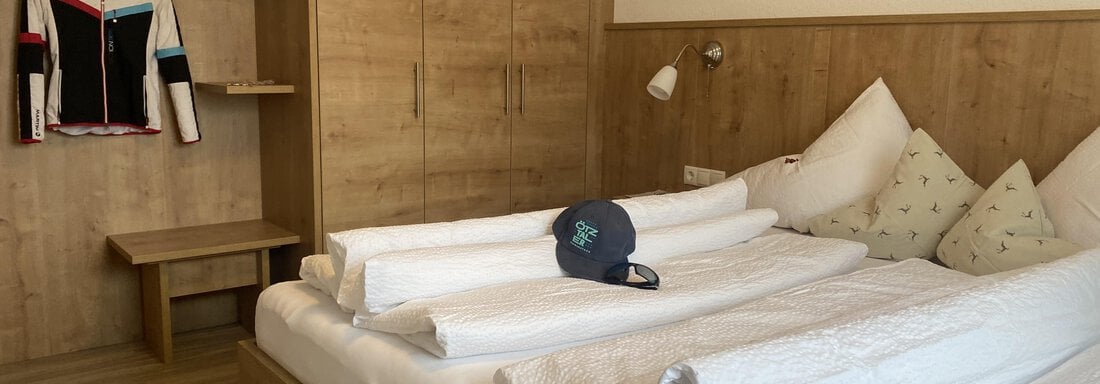 A cozy bedroom with a double bed and wood paneling. A jersey and a hat hang on the wall above a nightstand. - Sportpension Rubin - Sölden