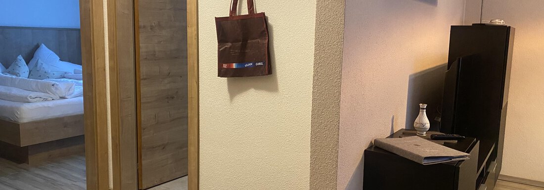 A cozy entrance area with wood laminate and a wardrobe. In the background is a bedroom with a bed and blue light. - Sportpension Rubin - Sölden