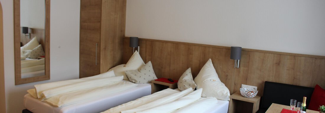 Zimmer A bright room with two single beds and modern furnishings. A table with chairs and a large mirror wall complete the space. - Sportpension Rubin - Sölden