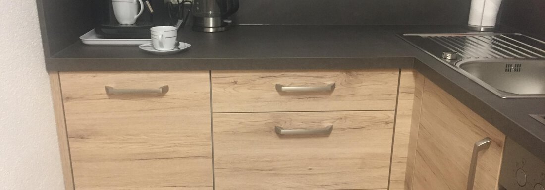 A modern kitchen with wooden and stainless steel surfaces. On the countertop, there is a fully automatic coffee machine and a coffee cup. - Sportpension Rubin - Sölden