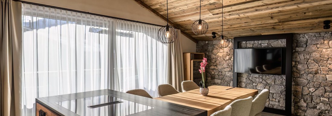 Black Stone (12) A modern kitchen with wooden ceilings and a dining area. Large windows provide plenty of natural light and a view of the landscape. - The Peak Sölden - Sölden