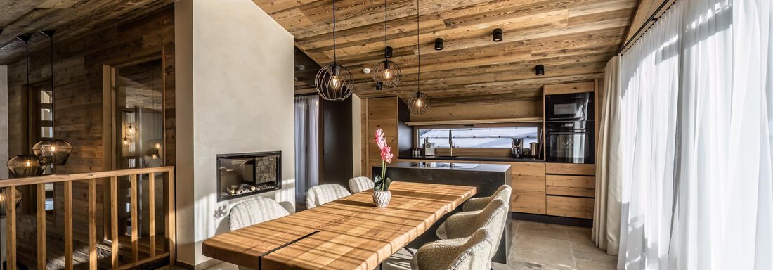 A modern dining room with a large wooden table and comfortable chairs. The walls are made of wood and the room light is warm and inviting. - The Peak Sölden - Sölden