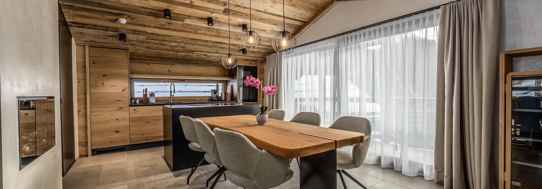 A modern dining room with a wooden table and comfortable chairs. Large windows let in a lot of light and offer a view outside. - The Peak Sölden - Sölden