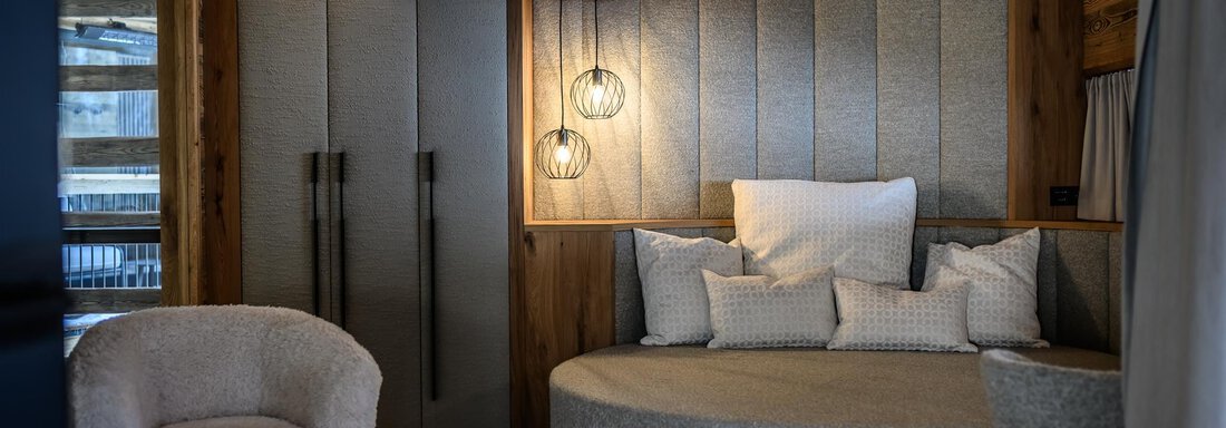 A stylish room with a round sofa, soft cushions, and a modern armchair. Wood paneling and cozy lighting create an inviting atmosphere. - The Peak Sölden - Sölden