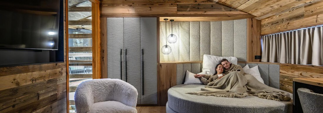 A cozy room with wood paneling and a round bed. Two people are relaxing on the bed in a warm and inviting atmosphere. - The Peak Sölden - Sölden
