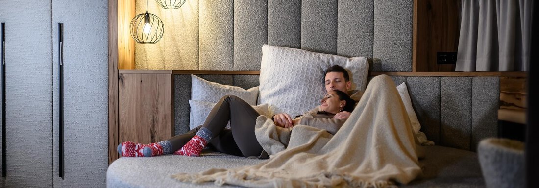 A cozy room with a round bed, where a couple is relaxing. The warm lights create an inviting atmosphere. - The Peak Sölden - Sölden